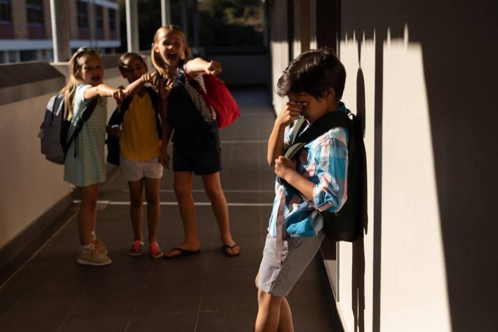 Front view of school friends bullying a crying boy in hallway of elementary school